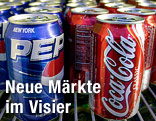 Dosen von Coca-Cola und Pepsi stehen in einem Kühlregal.