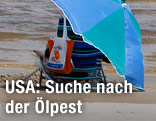 Jemand sitzt mit Sonnenschirm am Strand, daneben liegt ein Schwimmgurt