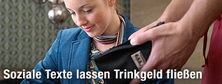 Eine Frau kramt in einer Geldbörse und ein Kellner hält ihr seine Brieftasche hin.