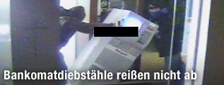 Ein Maskierter kippt einen Bankomaten um.