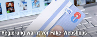 Eine Hand h&auml;lt eine Kreditkarte vor einem Webshop am Notebookbildschirm.