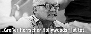 Filmproduzent Dino de Laurentiis sitzt auf einem Regiestuhl und raucht