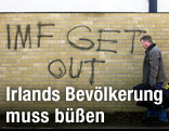 Ein Mann geht an einer Mauer vorbei, an der "IMF get out" gesprayt ist