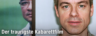 Der Deutsche Kabarettist Michael Mittermeier steht vor einem Bild von Zarganar, auf dem man nur eine Hälfte seines Gesichtes erkennt