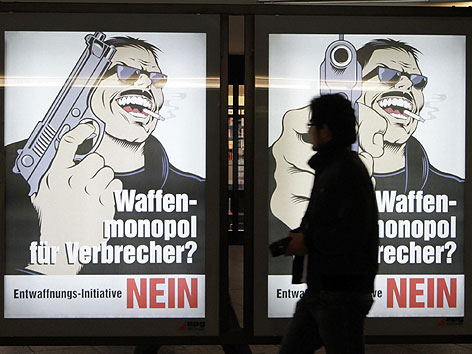 © APA/KEYSTONE/Peter Klaunzer Ein Passant läuft an Plakaten der Gegner der Waffenschutz-Initiative vorbei.