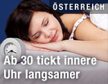 Frau schläft mit Wecker im Vordergrund