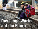 Zwei Kinder sitzen auf einem Bahngleis