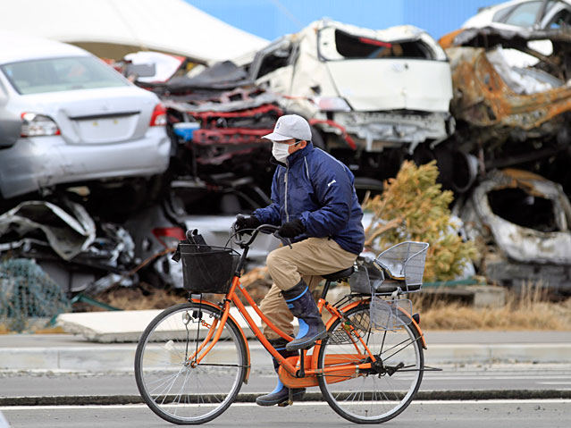 © APA/EPA/Stephen Morrison Ein Radfahrer fährt an einem Berg von Autowracks vorbei.