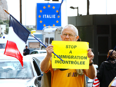 © AP/Antonio Calanni Franzose steht mit Flagge und Schild in der Hand, mit der Aufschrift "Stop a l'immigration incontrolee" vor der französisch-italienischen Grenze