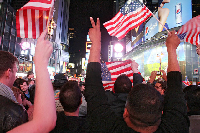 Menschen halten amerikanische Flaggen auf dem Times Square in die Höhe