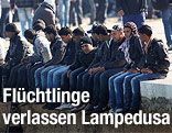 Fl&uuml;chtlinge sitzen an Hafen von Lampedusa