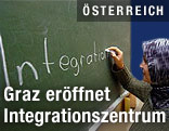 Frau mit Kopftuch schreibt das Wort "Integration" an eine Tafel