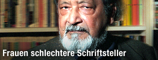 Sir V.S. Naipaul sitzt mit skeptischen Blick vor einem B&uuml;cherregal