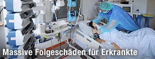 Eine Krankenschwester mit Mundschutz beugt sich im Krankenhaus &uuml;ber einen EHEC-Patienten.