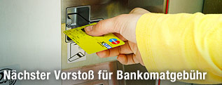 Hand steckt eine Karte in den Bankomat