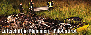 Feuerwehrleute tragen neben der Absturzstelle des ausgebrannten Luftschiffs einen Sarg.