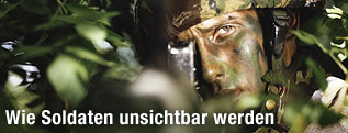 Ein im Gebüsch versteckter Soldat im Tarnanzug und bemaltem Gesicht