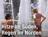 Zwei Personen im Badeanzug stehen vor einem Springbrunnen