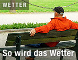 Mann sitzt mit Jacke auf einer Parkbank