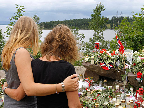 © AP/Ferdinand Ostrop Zwei junge Frauen stehen Arm in Arm und blicken auf Blumen und Kerzen.