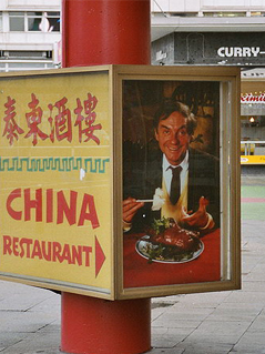 © Wikipedia/Sir James Leuchtkasten im Berliner Westen mit Wegpfeil zu einem China Restaurant und einem Porträt von Harald Juhnke
