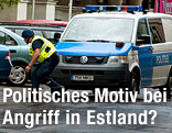 Ein Polizist geht geduckt vor einem Polizeifahrzeug