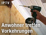 Person schraubt ein Brett an eine Hauswand