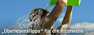 Frau leert sich einen Eimer voll Wasser über den Kopf