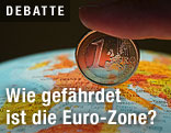 Finger hält eine Euromünze auf einen Globus