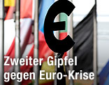 Eine Statue hält ein Euro-Zeichen vor verschiedenen Flaggen im Hintergrund