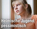 Junge Frau schaut nachdenklich aus dem Fenster