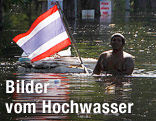 Ein Mann h&auml;lt im Hochwasser eine thail&auml;ndische Flagge hoch