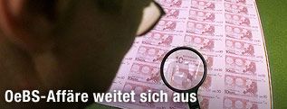 Ein Mann mit Lupe &uuml;berpr&uuml;ft frisch gedruckte Zehn-Euro-Scheine.