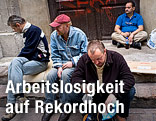 Drei Männer sitzen auf einem Gehsteig