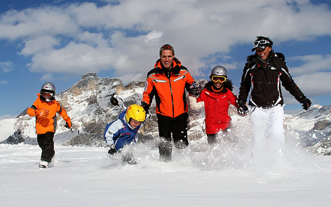 Eine Familie mit Kindern läuft lachend durch Tiefschnee