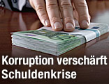 Ein Mann hat die Hand auf vielen Hundert-Euro-Scheinen auf einem Schreibtisch