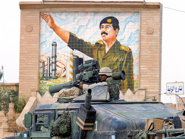 © Reuters/Nikola Solic Ein gepanzertes Fahrzeug der US-Armee fährt an einem Bild von Saddam Hussein vorbei