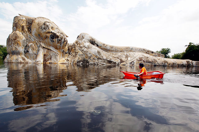 Mann in einem Boot vor einer zur Hälfte im Wasser liegenden Buddhastatue
