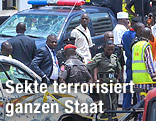 Sicherheitskr&auml;fte mit Polizeiauto neben einem durch eine Bombe besch&auml;digten Fahrzeug