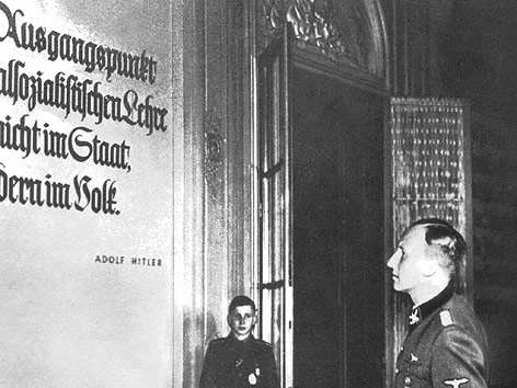 Reinhard Heydrich betrachtet bei einem Besuch der Ausbildungsschule des SIcherheitsdienstes in Prag ein Zitat von Adolf Hitler