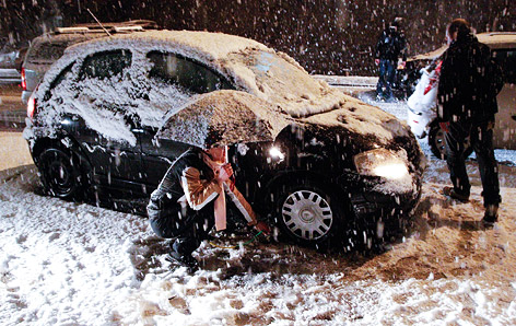 Frau versucht im Schneegestöber Schneeketten an ihr Fahrzeug anzubringen