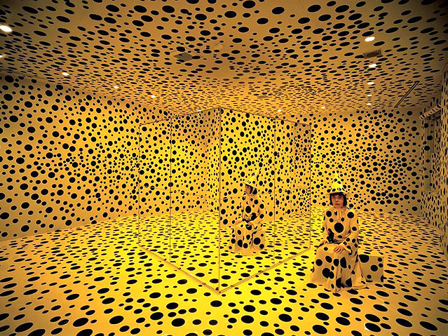 © APA/Kunsthalle Wien Yayoi Kusama in gelbem Kleid und Hut mit schwarzen Tupfen in einem gelben Raum mit schwarzen Tupfen