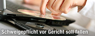 Eine Hand legt eine DVD in das ge&ouml;ffnete Einschubfach eines Laptops