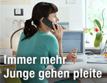 Junge Frau sitzt zu Hause an ihrem Schreibtisch und telefoniert