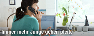 Junge Frau sitzt zu Hause an ihrem Schreibtisch und telefoniert