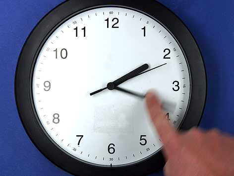 © APA/dpa/Jens Büttner Ein Finger bewegt den großen Zeiger einer Uhr