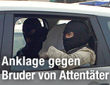 Zwei verhaftete Verdächtige sitzen vermummt in einem Polizeiauto