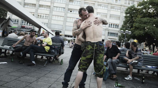 © Christian Reister Zwei Männer mit nacktem Oberkörper und Camouflage-Hosen umarmen einander.