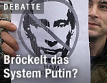 Das gezeichnete Gesicht Putins ist auf einem Plakat eines Demonstranten durchgestrichen