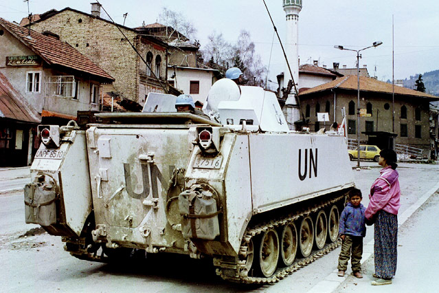 Ein Mädchen betrachtet mit ihrem kleinen Bruder an der Hand einen UN-Panzer